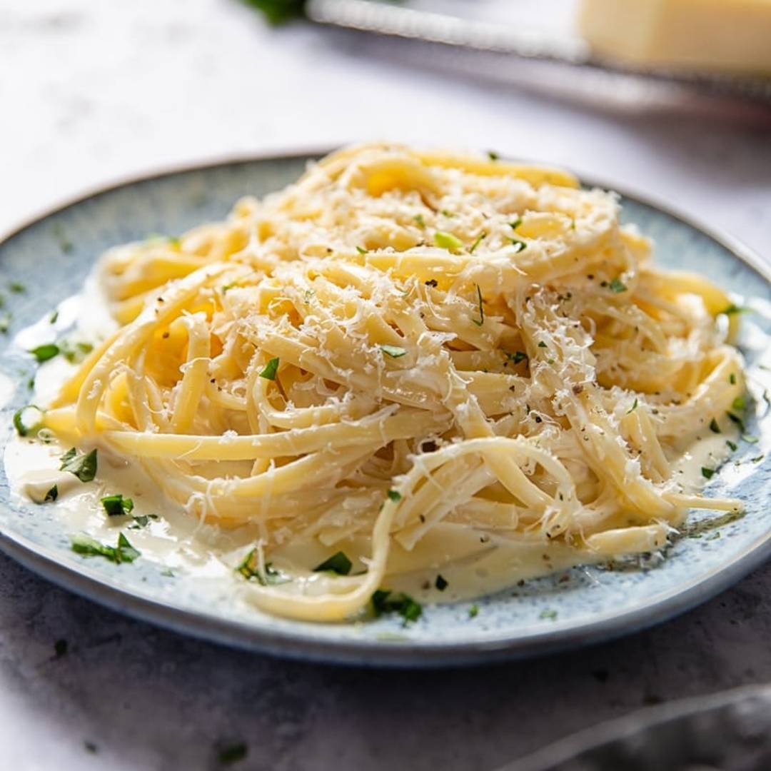 a plate with a bed of noodles in a white sauce with grated cheese and herbs