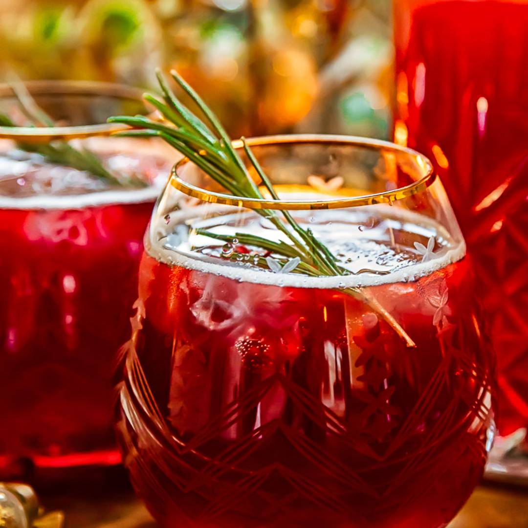 a gold rimmed glass with ice, a red fizzy drink and rosemary