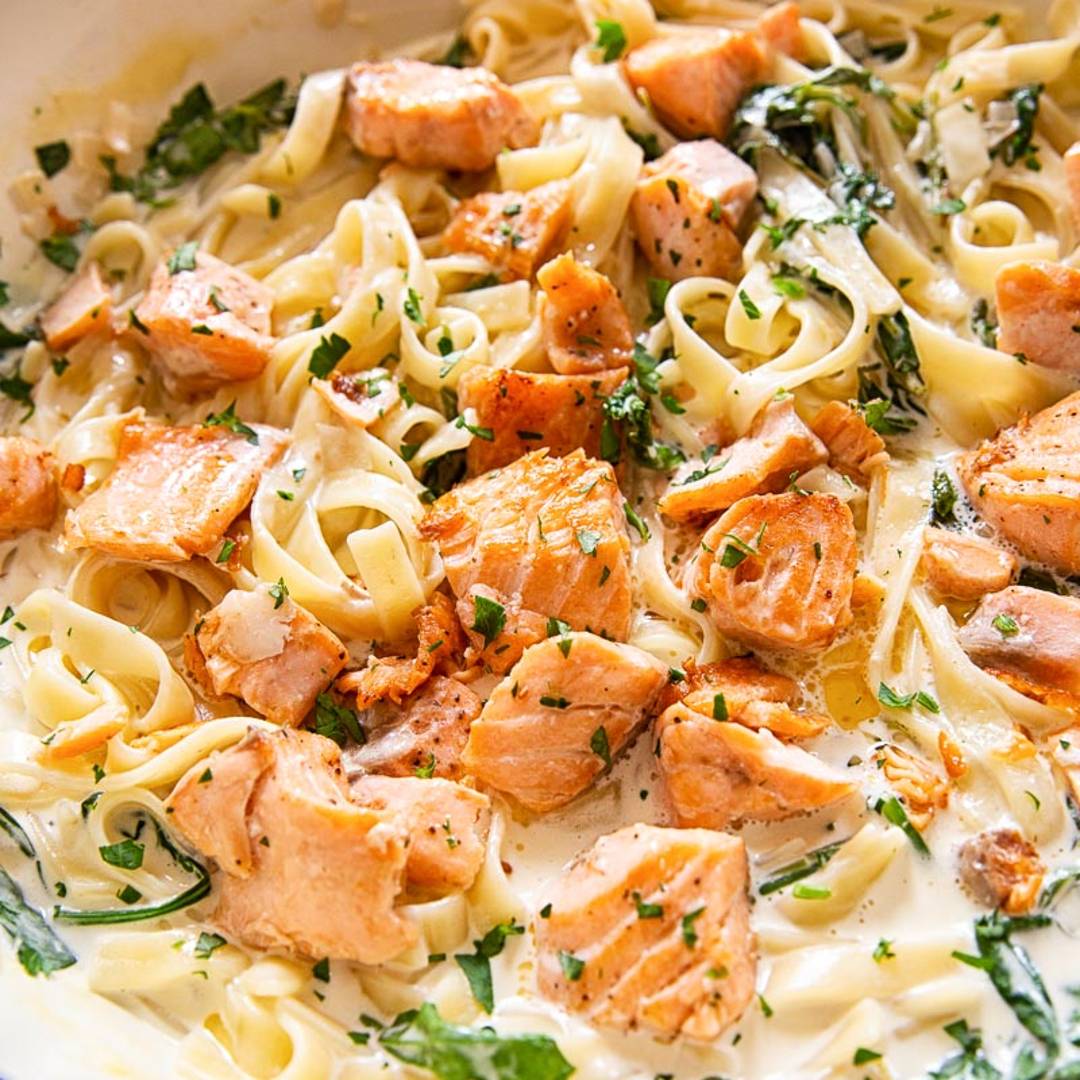 a deep pan with pasta and salmon chunks in a creamy sauce with herbs.