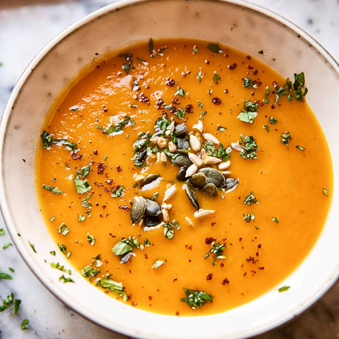 a white bowl of orange soup topped with seeds and herbs