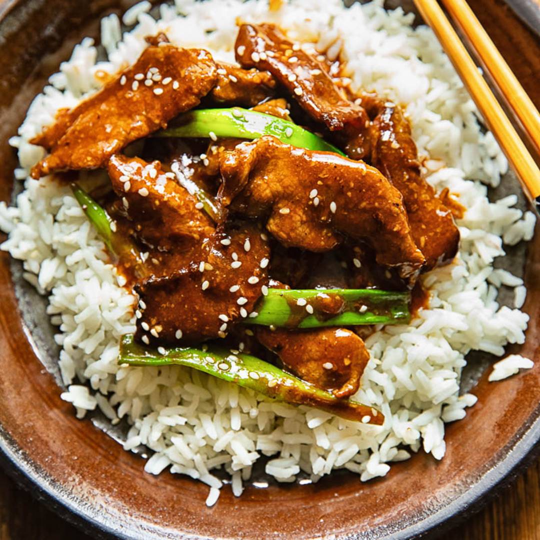 plate of white rice topped with strips of beef with a dark sauce, plus chopsticks