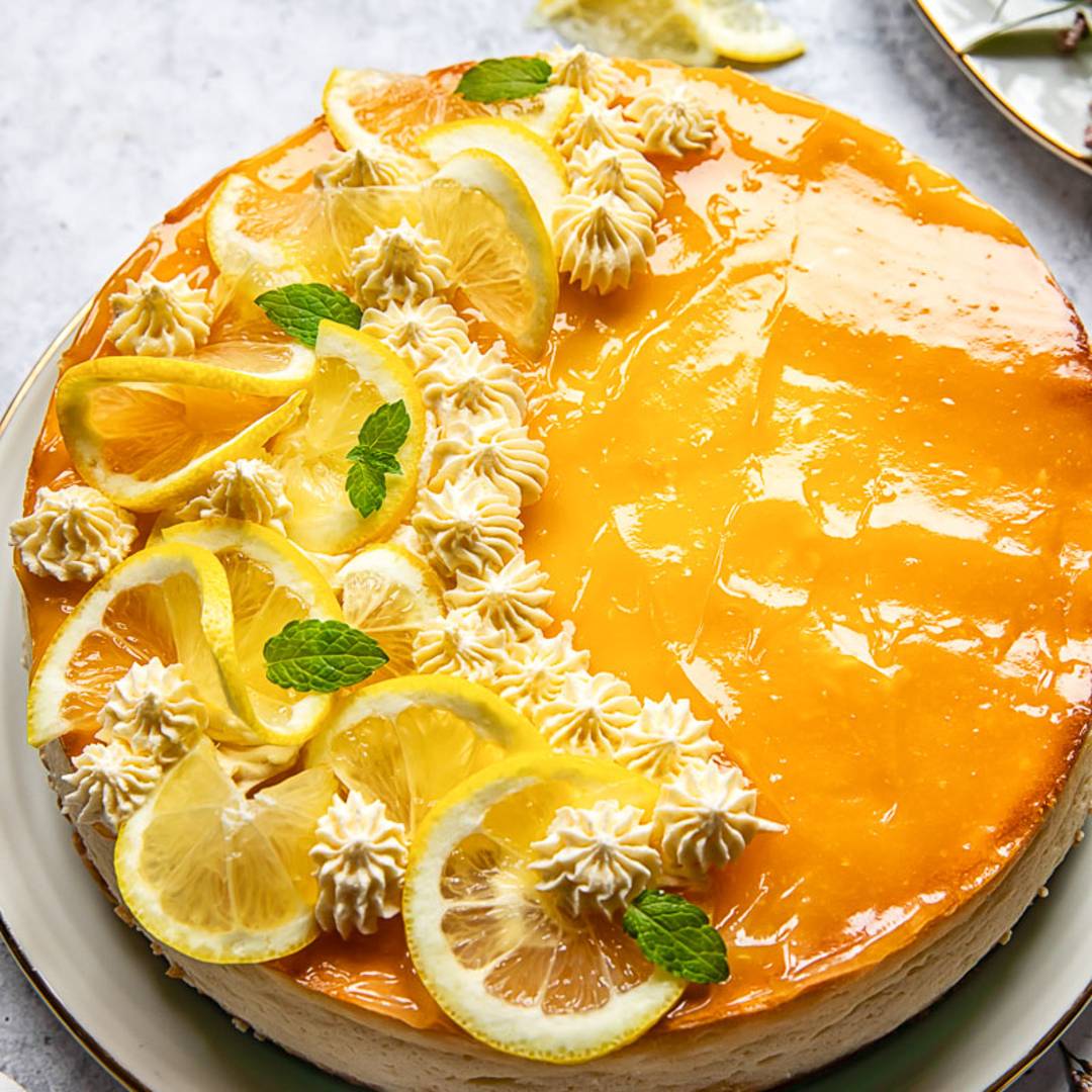 cheesecake on a platter, covered in lemon curd and decorated with lemon slices and icing pipettes