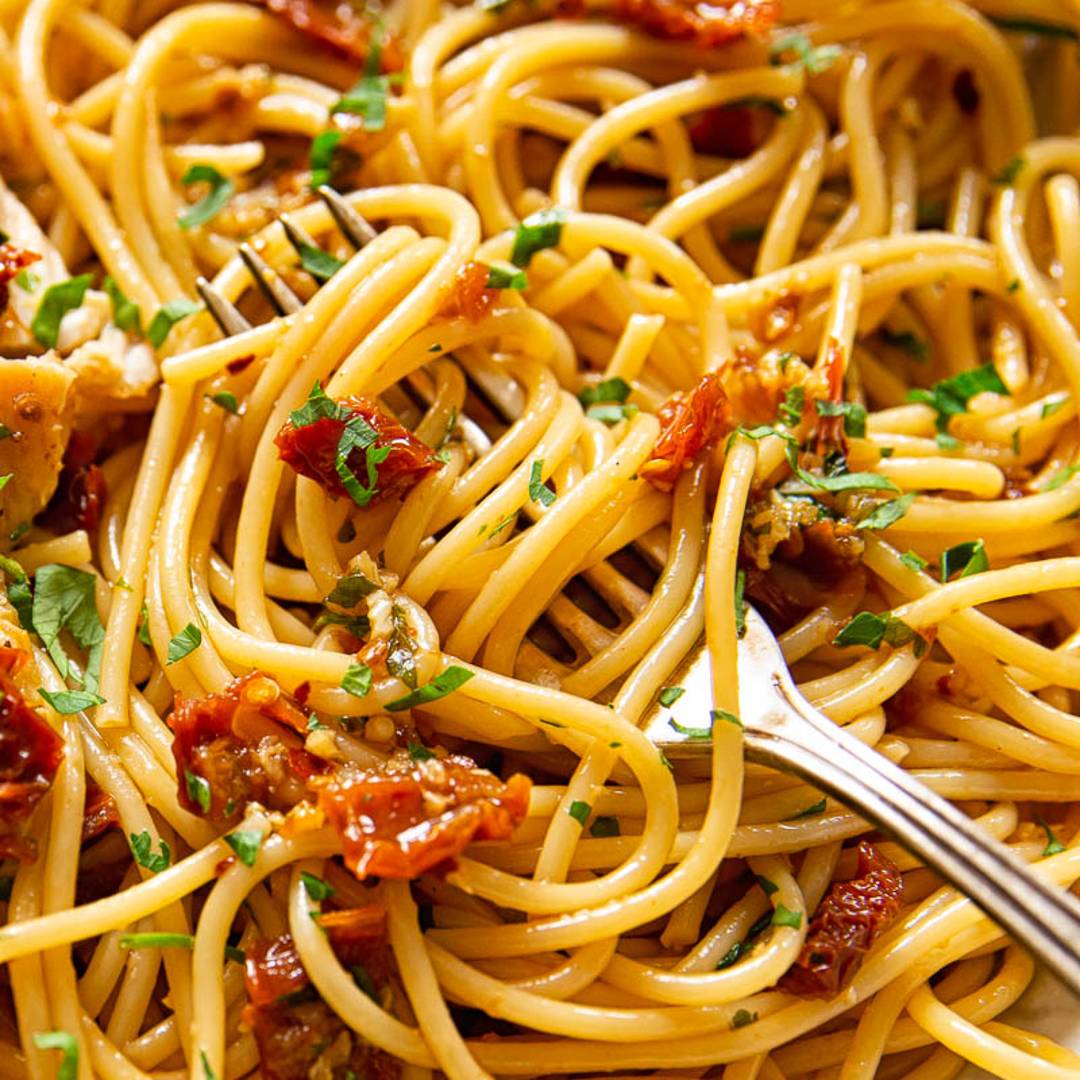 close up image of spaghetti with sun dried tomatoes and herbs with a fork