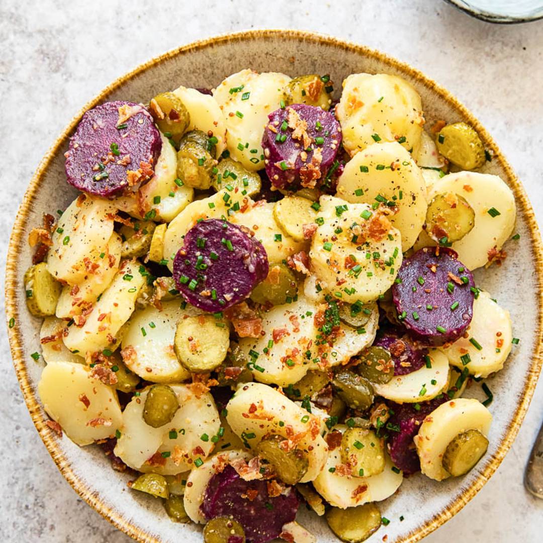 a white bowl with sliced potato, including purple potatoes, topped with spices