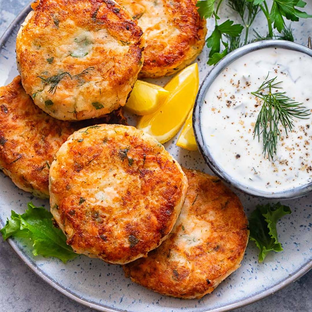 a plate of golden salmon cakes with a dipping sauce, lemon wedges and greens