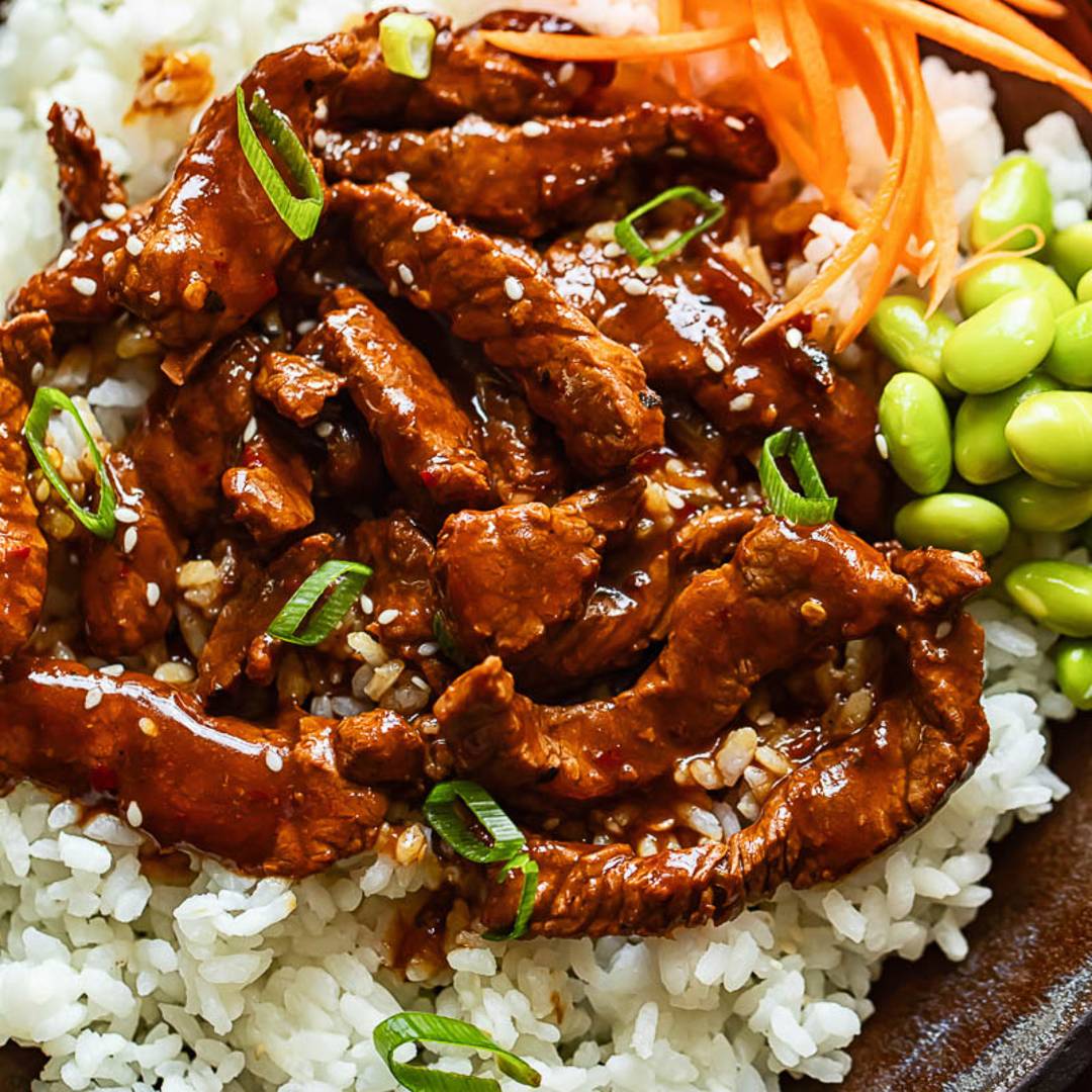strips of beef in sauce on rice with strips of carrot and edamame beans