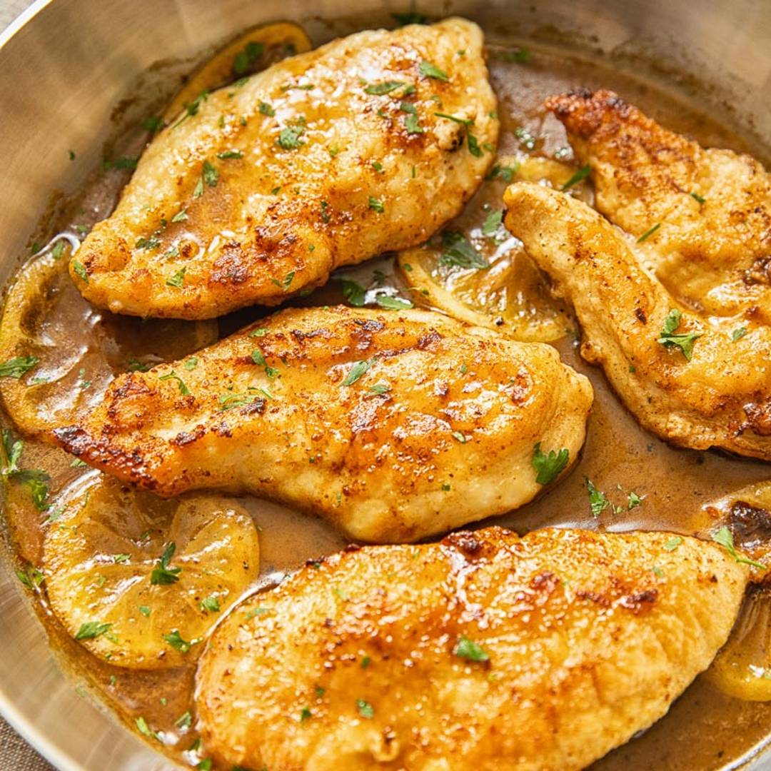 four chicken pieces in a stainless steel pan with a brown lemon sauce
