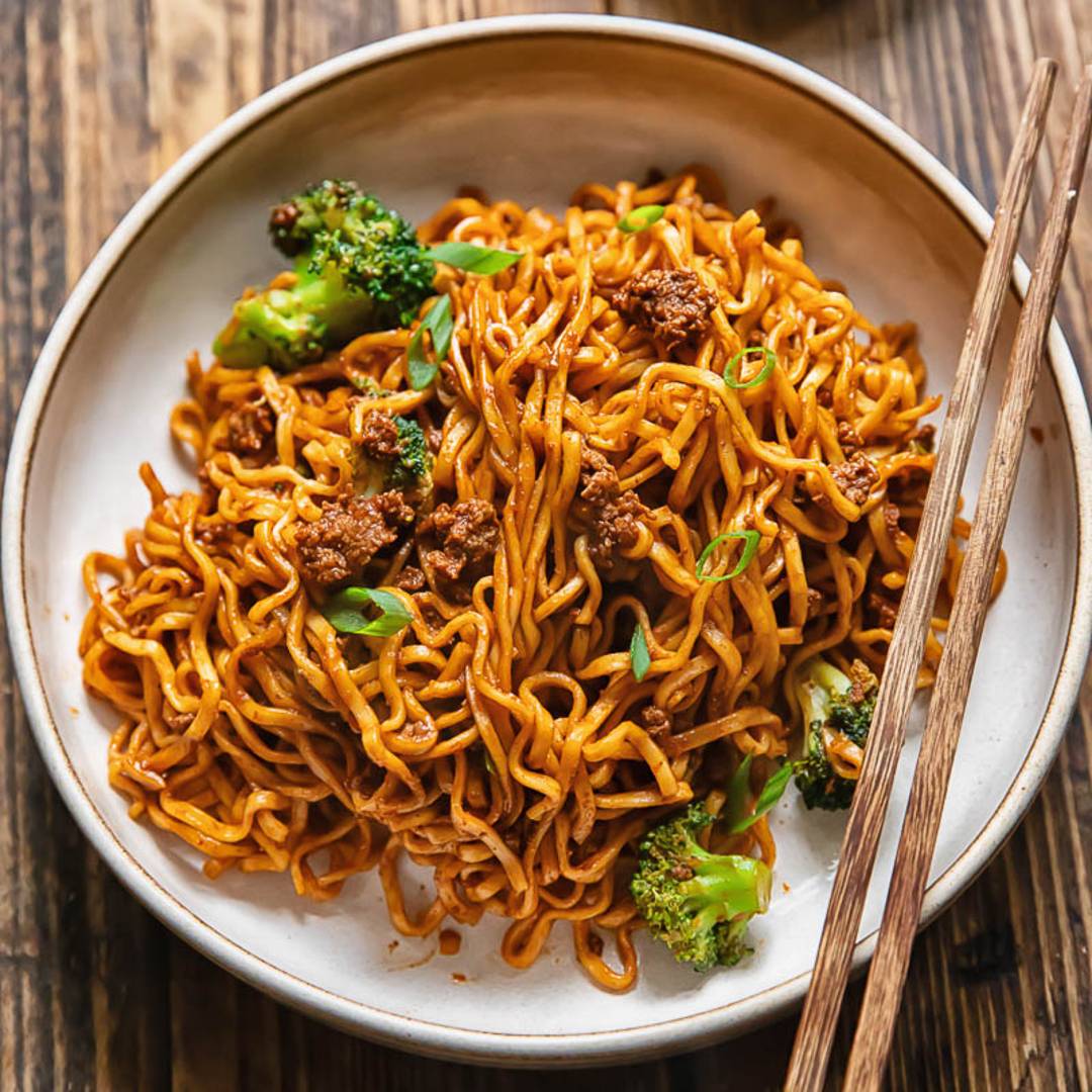bowl on a wood background with noodles and broccoli with two chopsticks