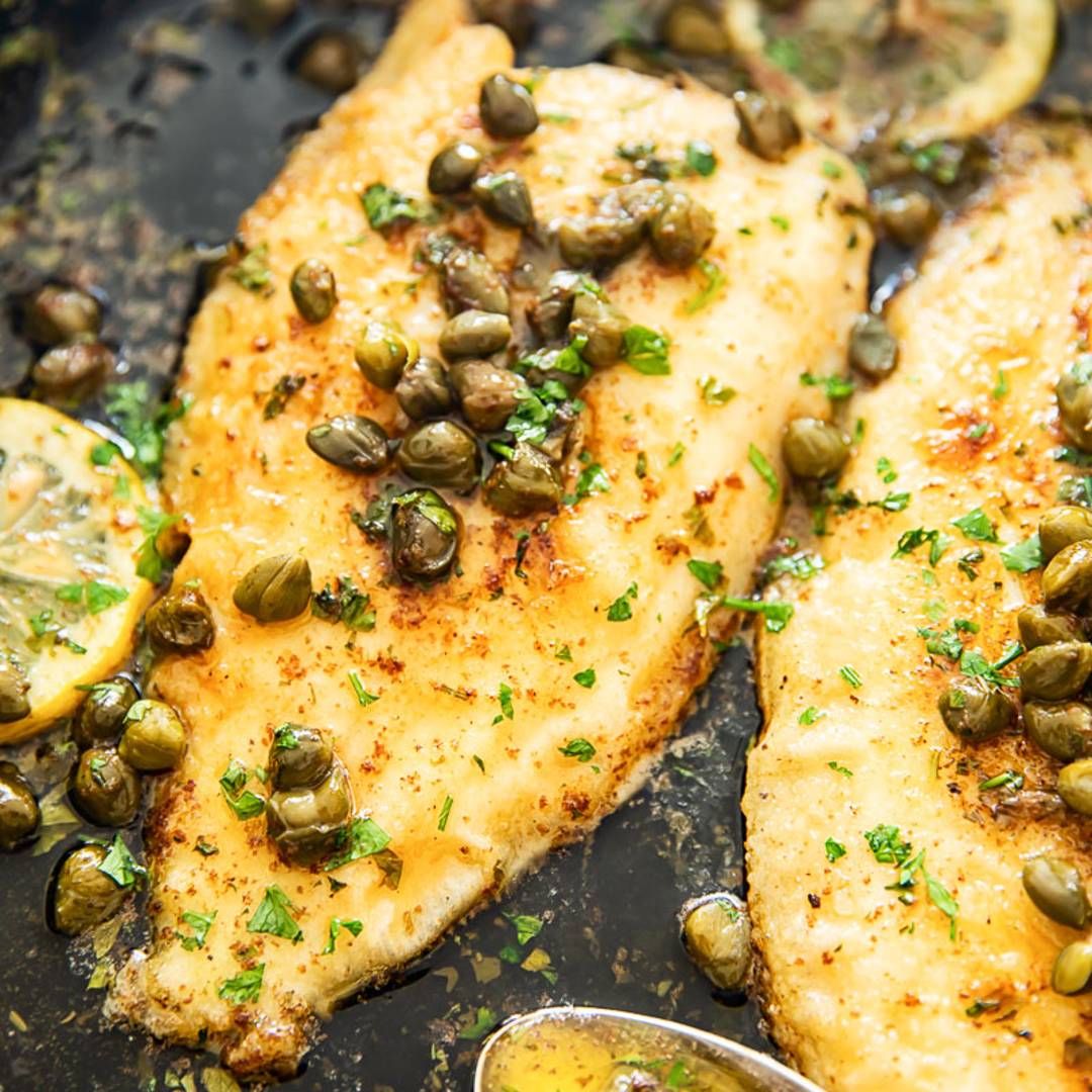 two pieces of white fish with oil, capers and herbs