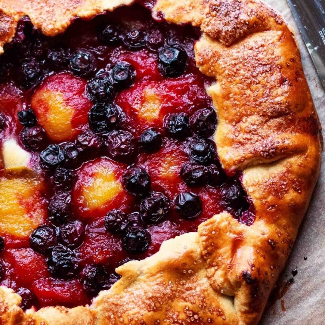 a rustic galette with plums and blueberries, with a golden crust, on a baking sheet.