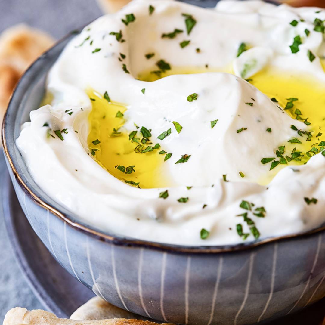 blue bowl filled with yogurt dip, with chives and olive oil, surrounded by grilled flatbread