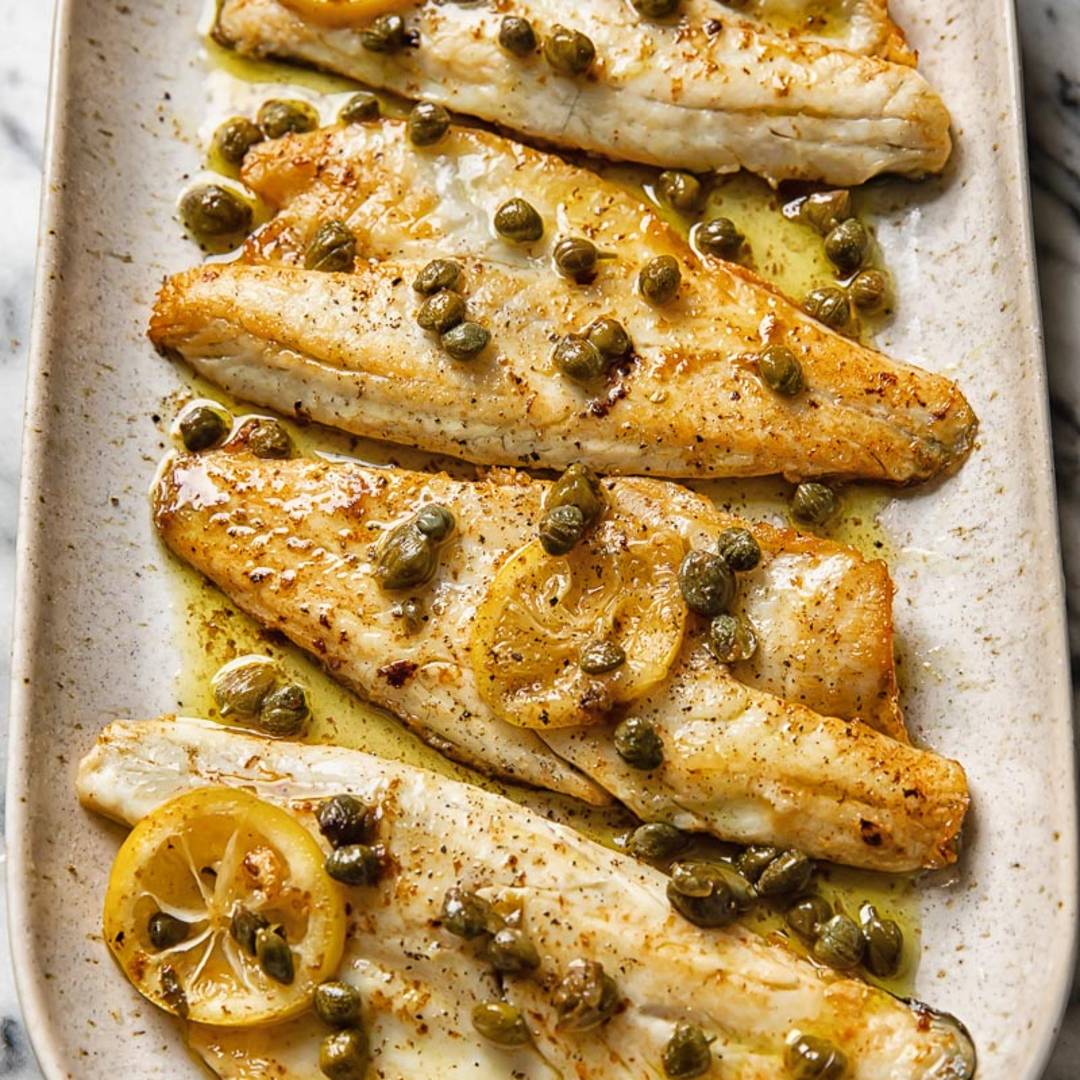 four pieces of sea bass on a platter with a golden sauce and a sprinkling of capers