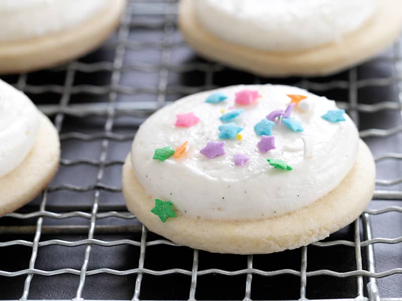 round sugar cookies with thick frosting and star sprinkles on wire rack