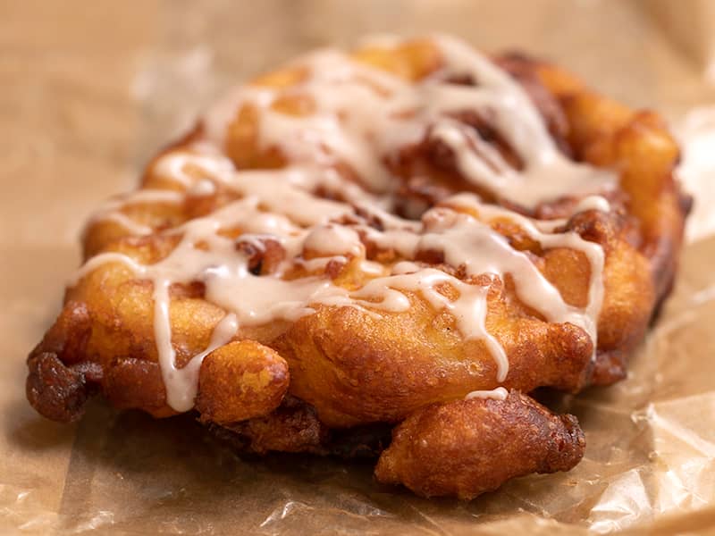 Apple fritter with glaze drizzle on brown paper