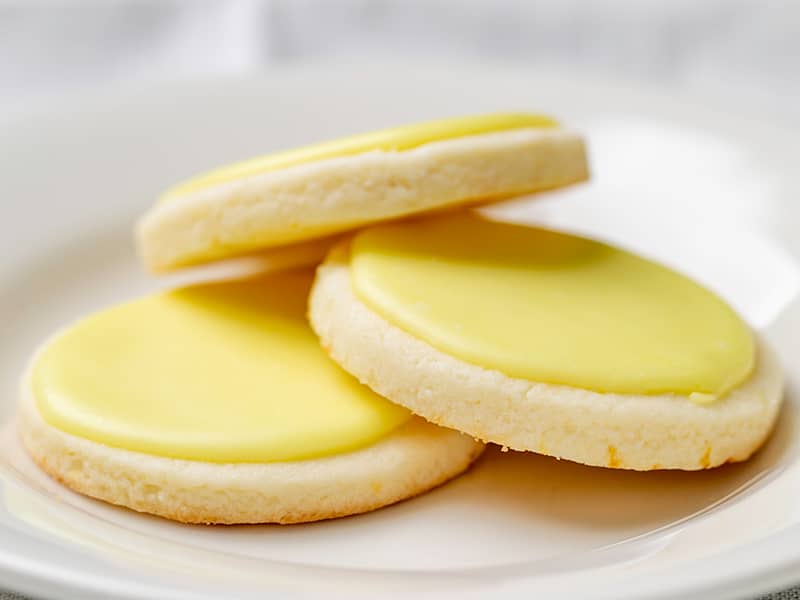 3 round pale round cookies with yellow flecks and bright yellow icing on small white plate