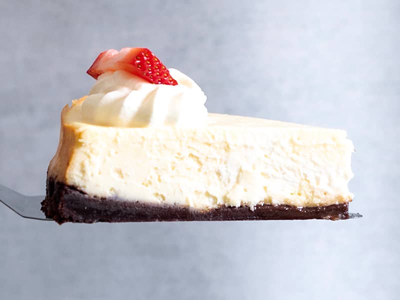 slice of cheesecake with whipped cream and a sliced strawberry on pie turner