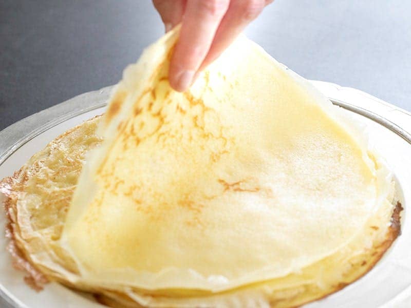 fingers picking up a light thin round pancake from large white platter