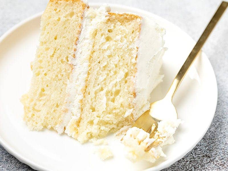 slice of vanilla cake with frosting on small white plate with fork