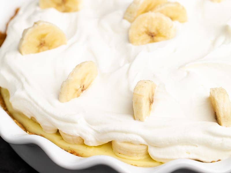 bananas in whipped cream on top of yellow custard in white pie plate