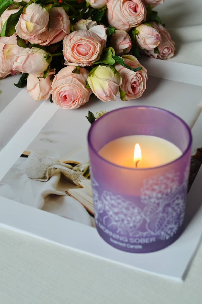 A lit candle and roses sit on a book.
