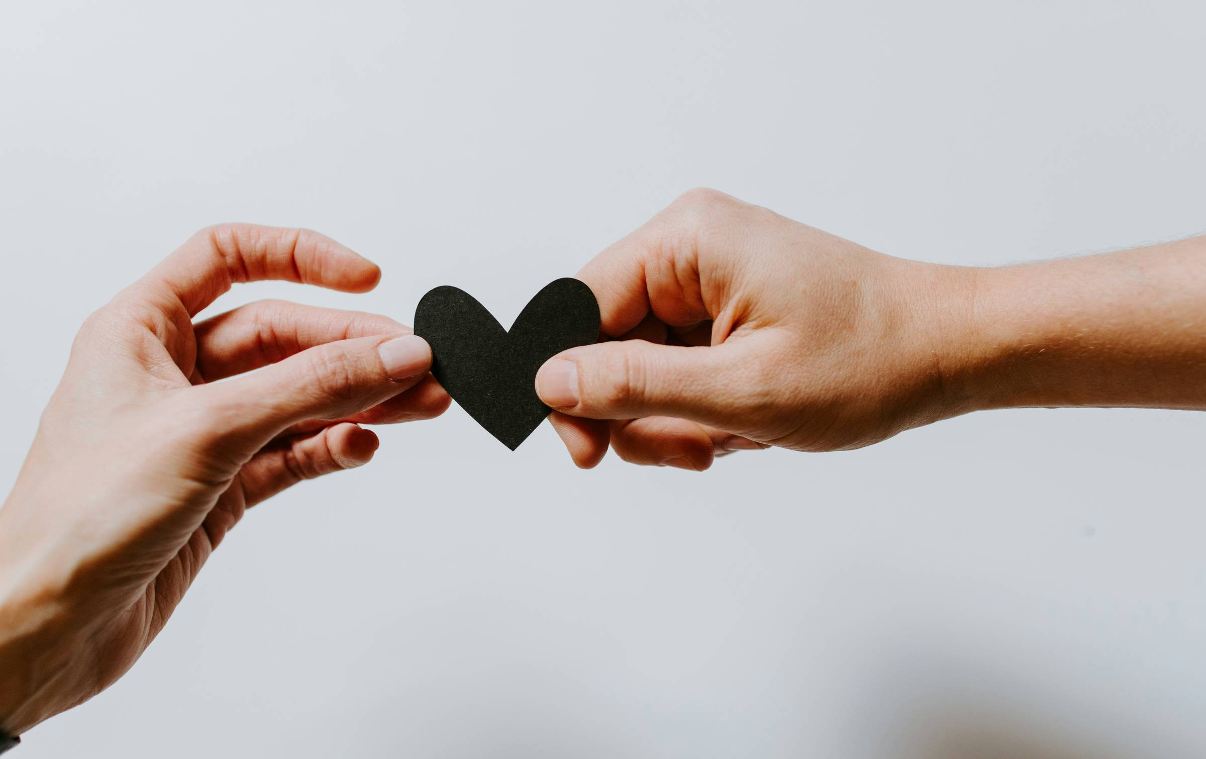 Two hands exchange a cut out heart in black. Sharing is Caring and Mental Health go hand in hand.