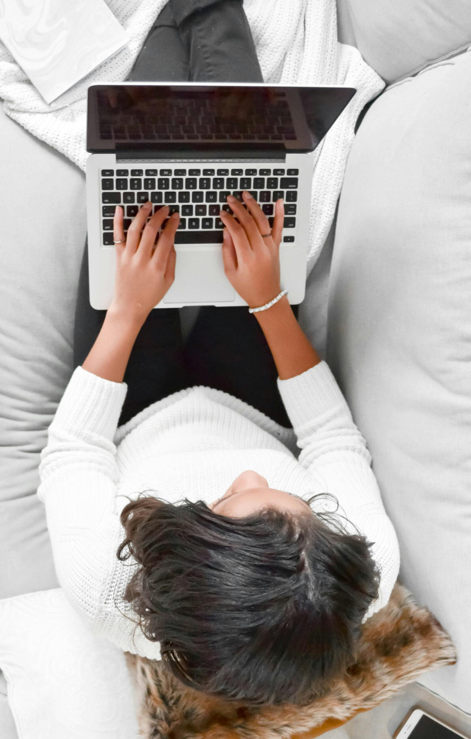 stock image of a picture taken above looking down at a woman sitting on her bed working on her laptop
