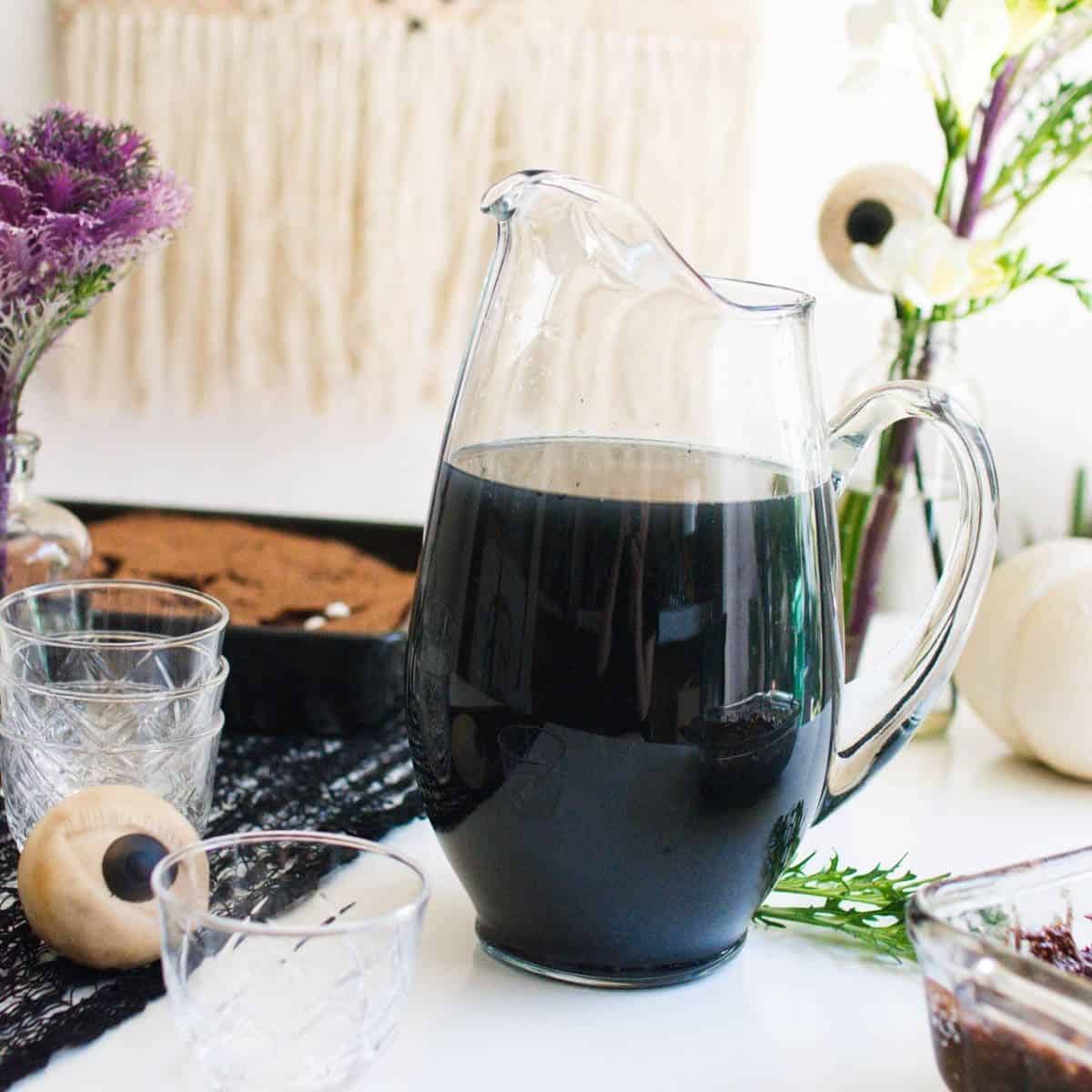 Black punch in a glass pitcher on a table with eyeball decorations for Halloween