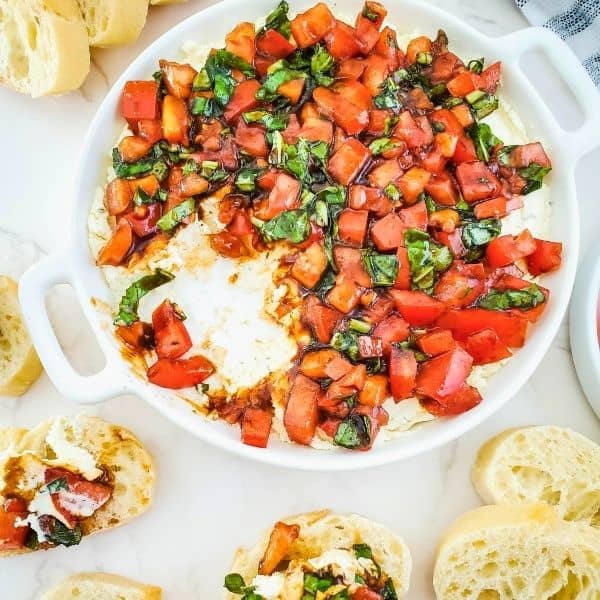 A white dish with boursin dip topped with bruschetta tomatoes.