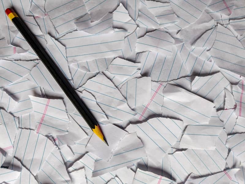 A pencil on a pile of torn, crumpled lined paper.