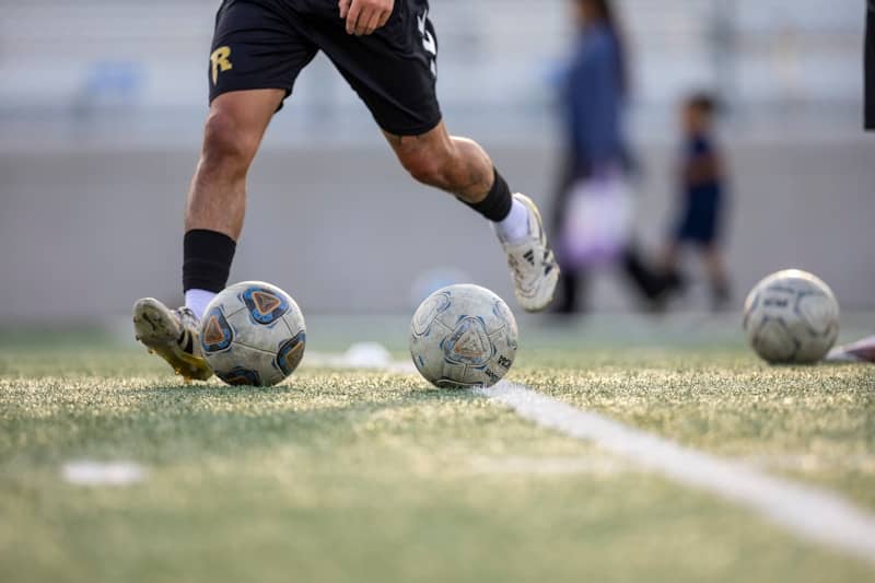 A soccer player practicing with balls on field