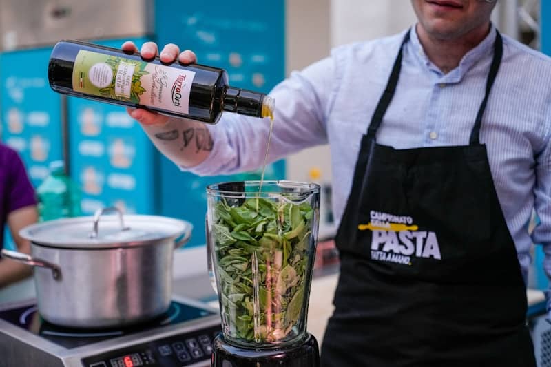 Chef preparing pesto by adding oil to basil in blender.