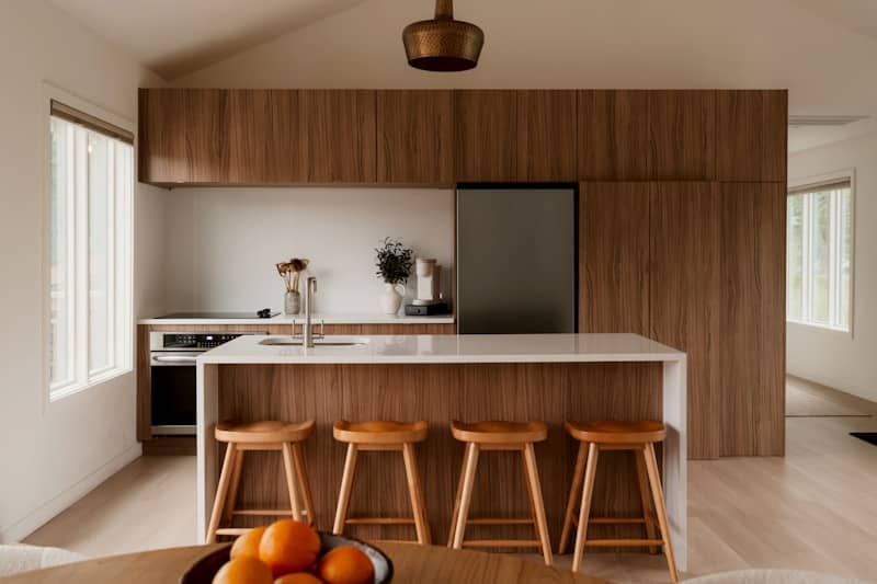 A modern kitchen with walnut cabinetry, a white island, and four wooden stools