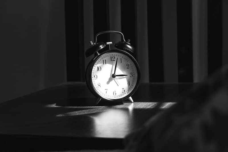 An analog alarm clock on a dark surface in a patch of light