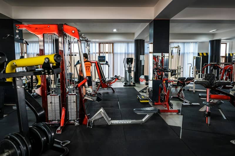 A person in an orange jersey exercising in a gym with red equipment