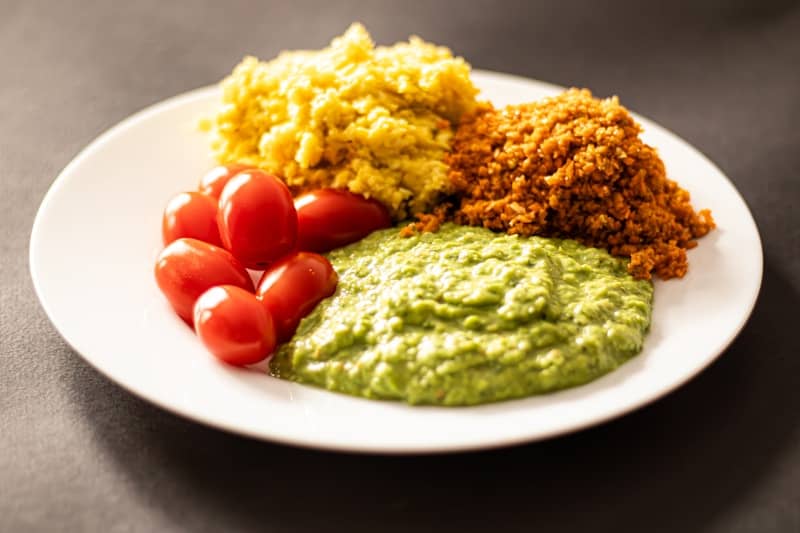 A plate with yellow, brown, green food and cherry tomatoes.