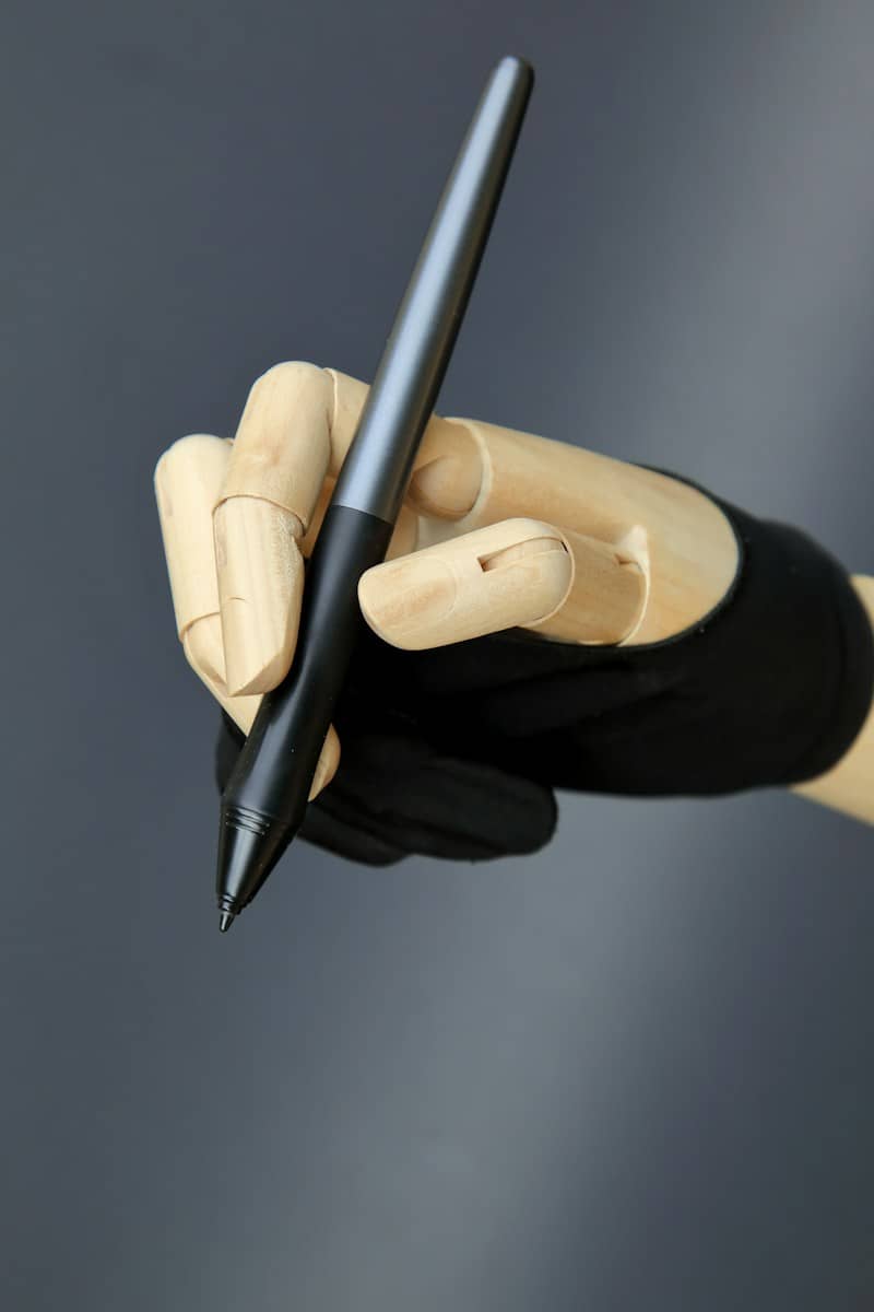 A wooden mannequin hand wearing a black glove holding a black stylus