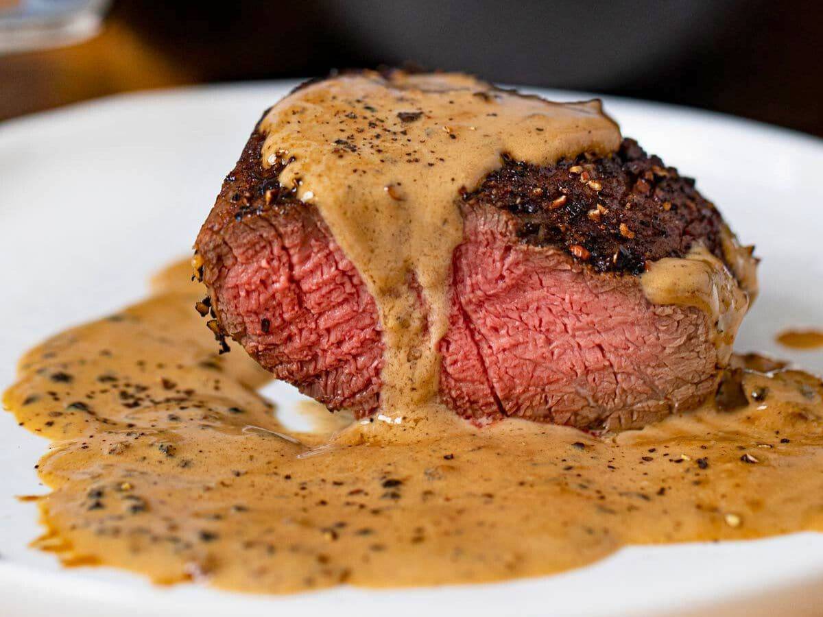 Perfectly cut piece of steak on a plate dripping with a light-brown pepper sauce
