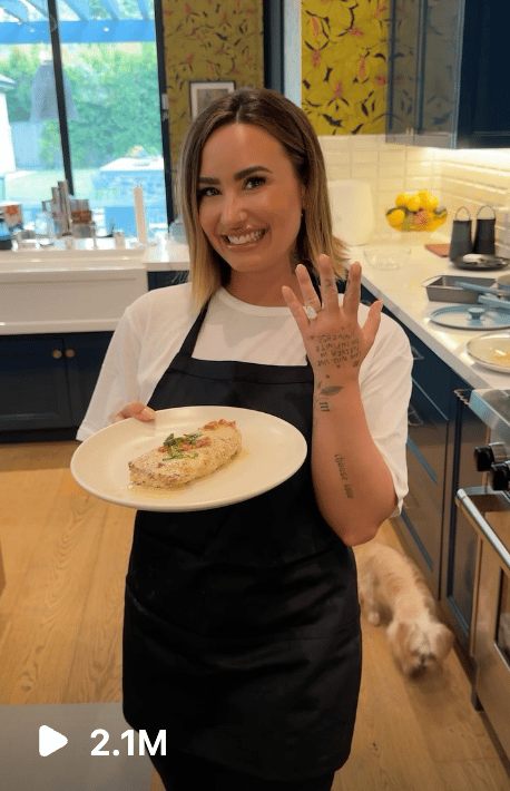 Demi lovato standing with a plate of marry me chicken, and showing off her engagement ring