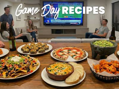 text: game day recipes; image: table full of party foods, group of people watching football in the background