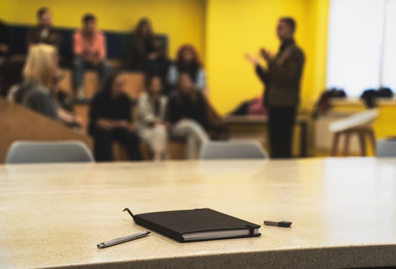 Notebook and pens on table with blurred audience and speaker