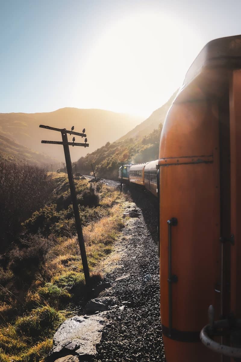 Train travels through a sunny mountain valley at sunset.