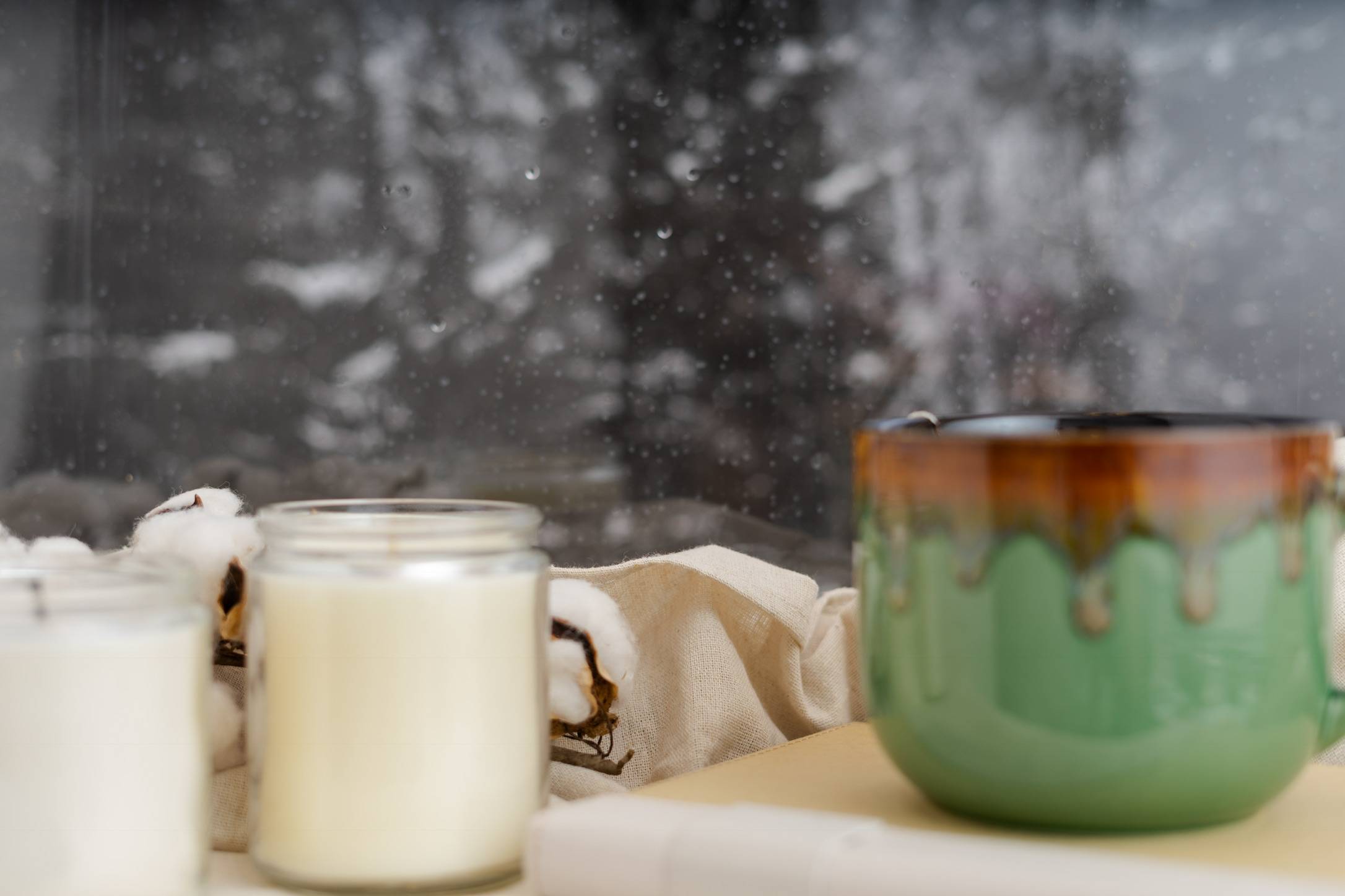 A mug of tea and candles in front of a rainy window