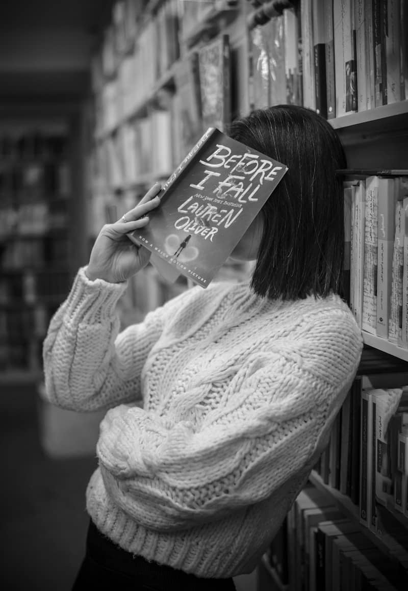 Woman hides her face behind a book in a library.