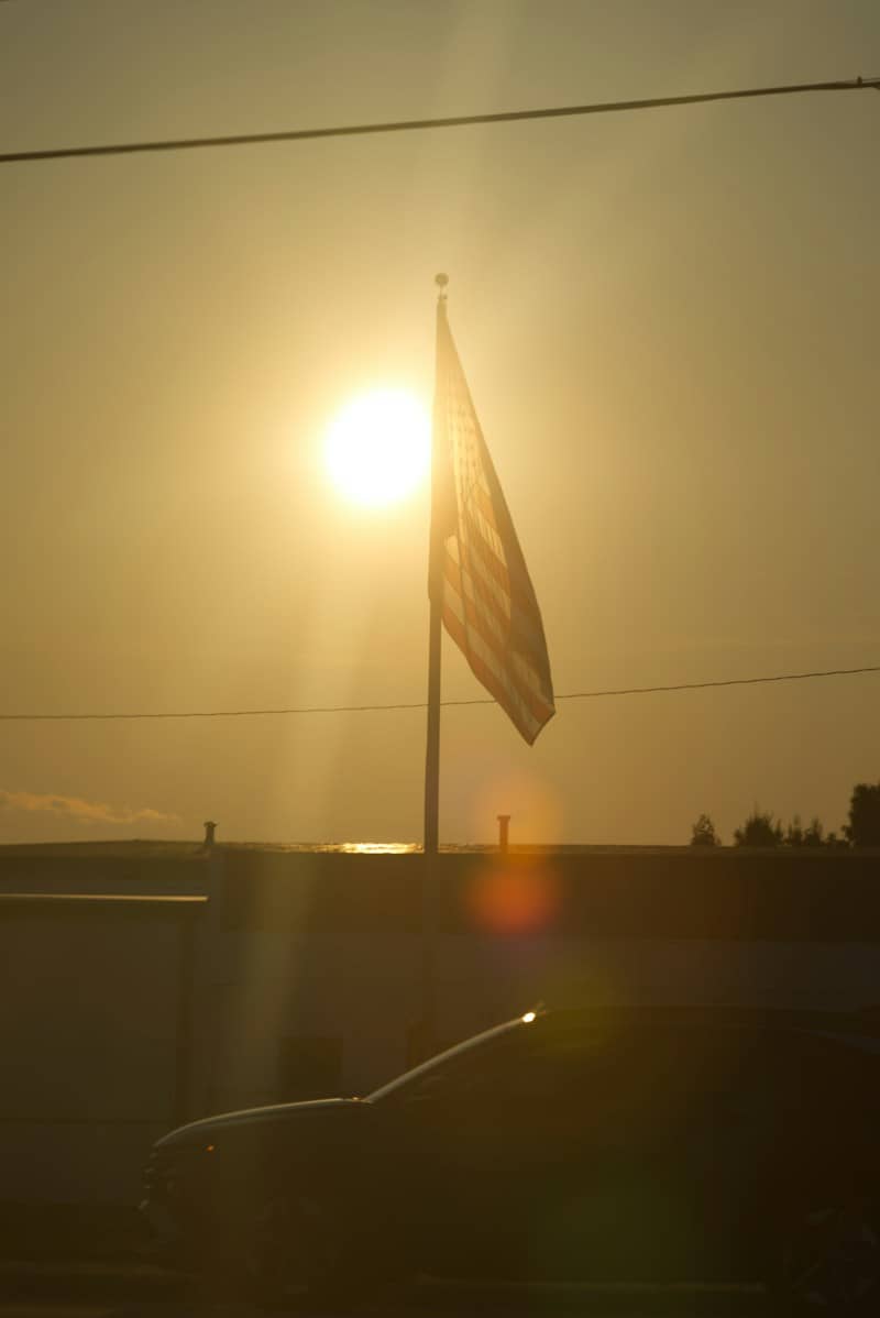 An American flag on a pole backlit by a low sun