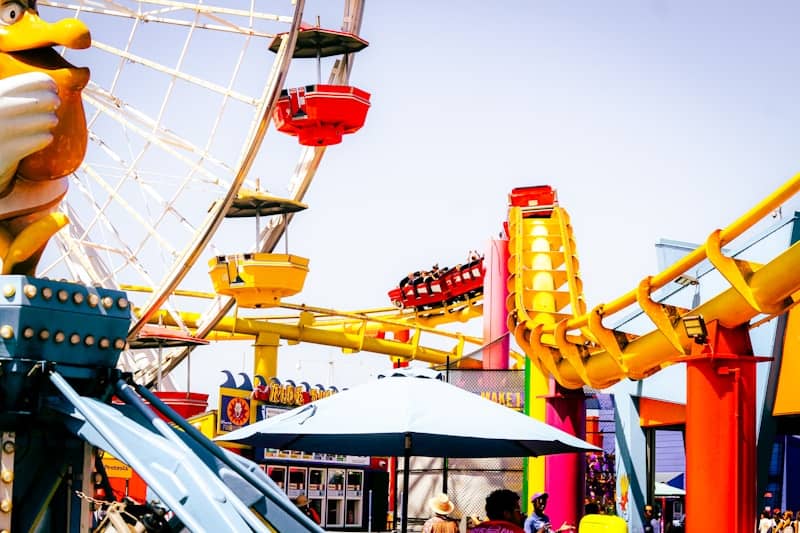 A red roller coaster car on yellow tracks beside a ferris wheel.