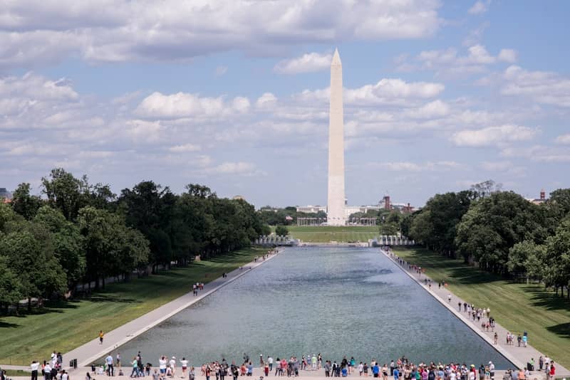 Washington monument and reflecting pool with people under blue sky.