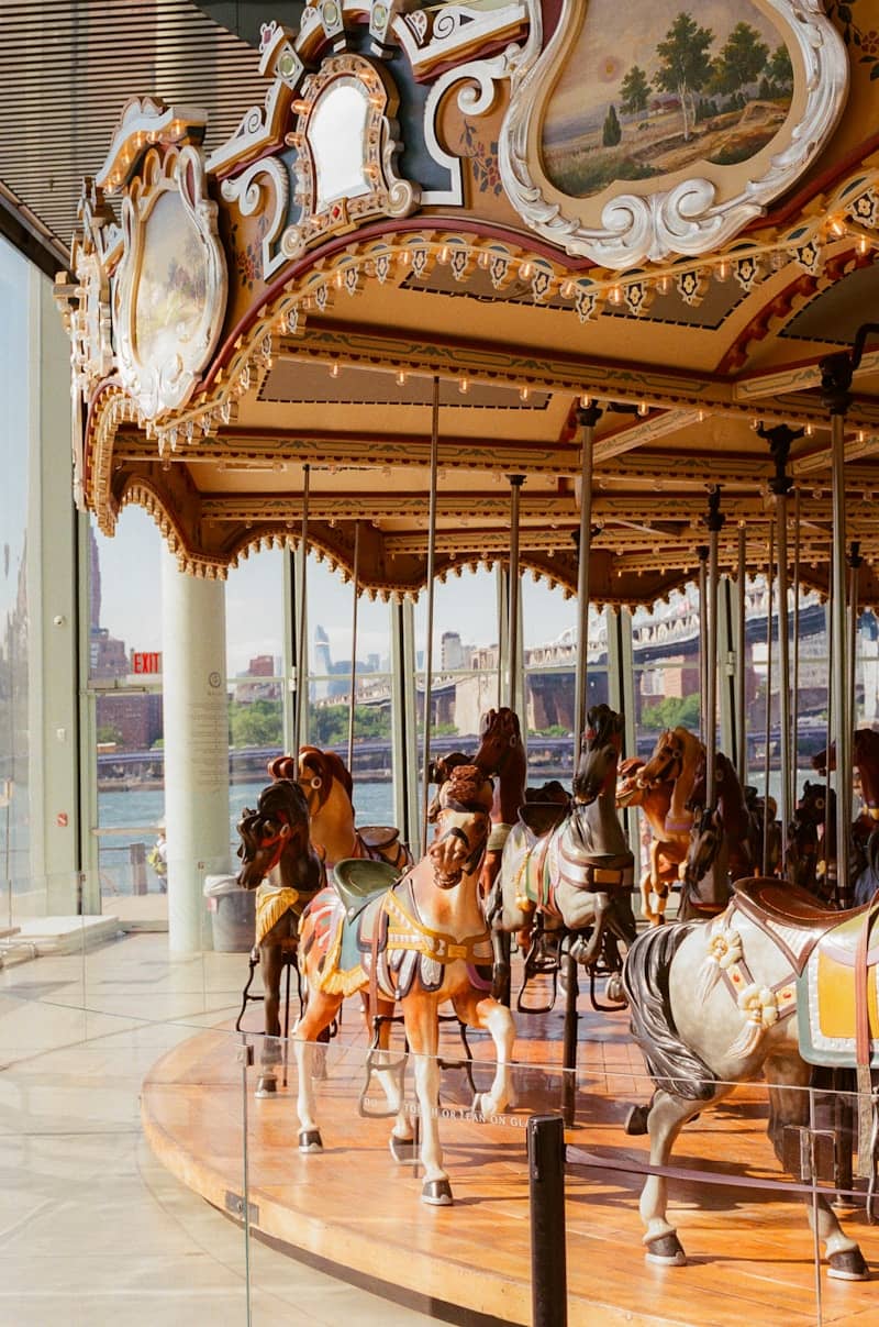 Ornate carousel horses in a glass pavilion overlooking a city.