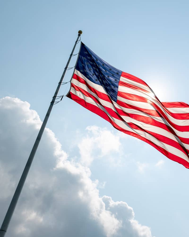 American flag waving on a flagpole under a sunny sky.