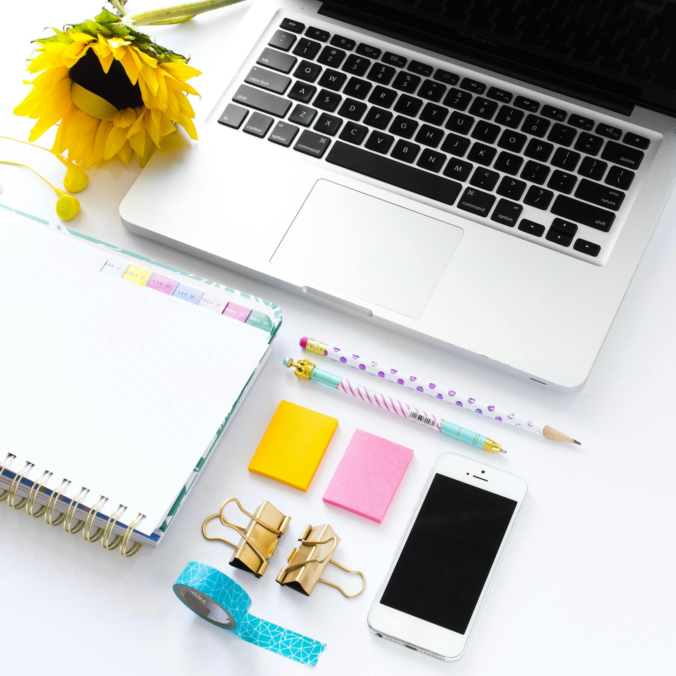 A white laptop with pencils, pad of paper, phone and other desk supplies