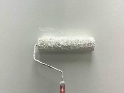 A paint roller on a white wall covered in white paint.